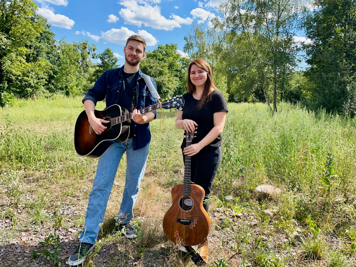 Ein Musiker und eine Musikerin mit Gitarren auf einer Wiese